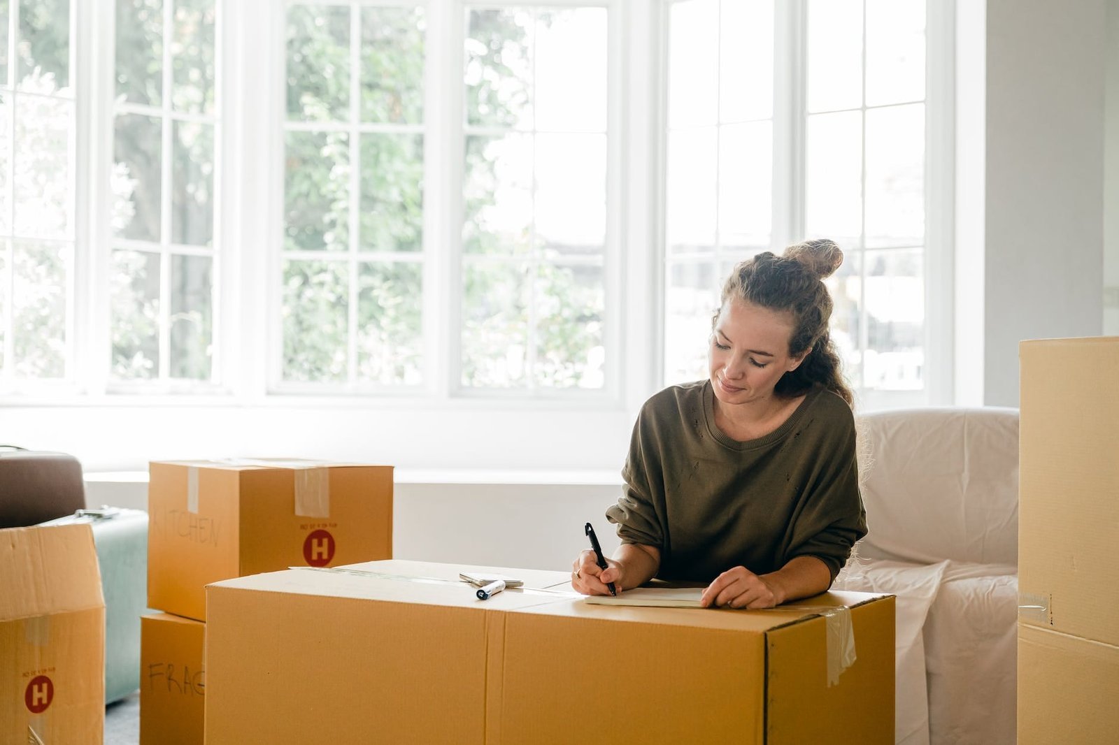 move-in process with woman signing box near large window in sunlight at home